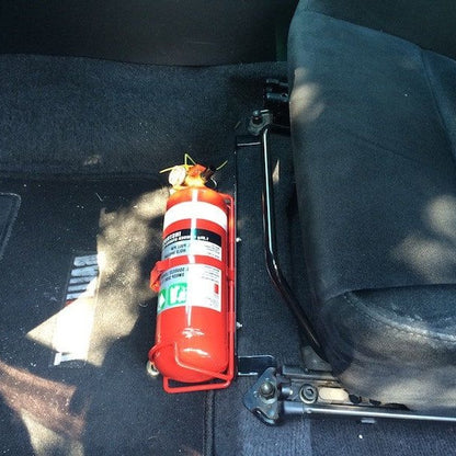 Close-up of a red fire extinguisher held in a KAP bracket at the base of the left front seat in a Mitsubishi Evo VIII