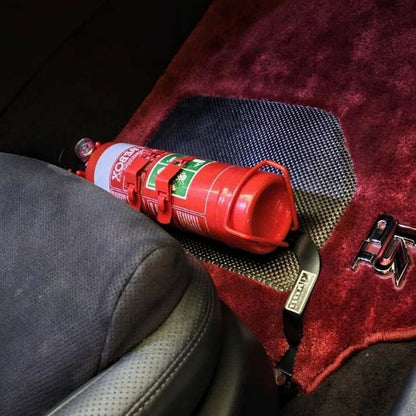 Close-up of a red fire extinguisher held in a KAP bracket at the base of the left front seat in a Nissan GT-R