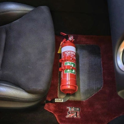 Close-up of a red fire extinguisher held in a KAP bracket at the base of the left front seat in a Nissan GT-R