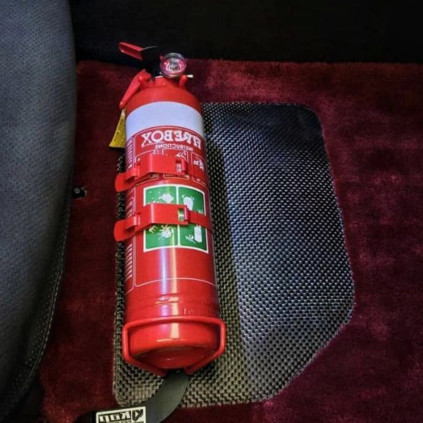Close-up of a red fire extinguisher held in a KAP bracket at the base of the left front seat in a Nissan GT-R