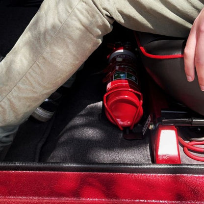 Person seated in a Suzuki Samurai, showing the foot room beside the fire extinguisher at the base of the front seat