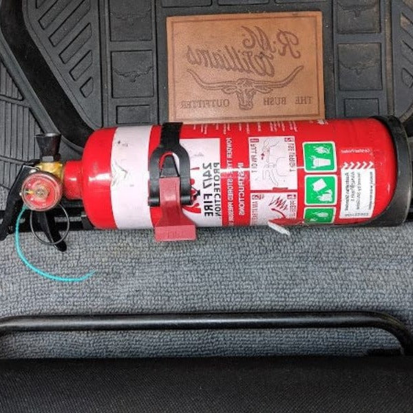 Close-up of a red fire extinguisher held in a KAP bracket at the base of the front seat in a Toyota LandCruiser 100 Series