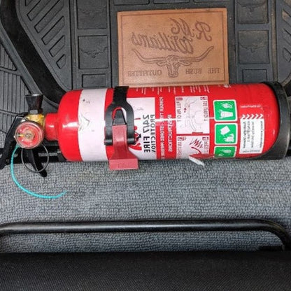 Close-up of a red fire extinguisher held in a KAP bracket at the base of the front seat in a Toyota LandCruiser 100 Series
