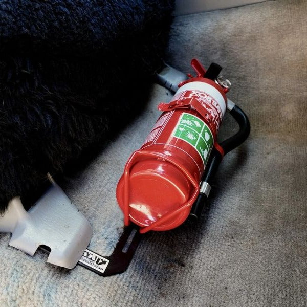 Close-up of a red fire extinguisher held in a KAP bracket at the base of the front seat in a Toyota LandCruiser 100 Series