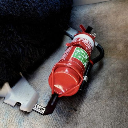 Close-up of a red fire extinguisher held in a KAP bracket at the base of the front seat in a Toyota LandCruiser 100 Series