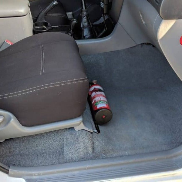 Toyota LandCruiser 100 Series cabin with a red fire extinguisher mounted on a KAP bracket at the base of the front seat