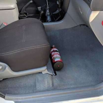Toyota LandCruiser 100 Series cabin with a red fire extinguisher mounted on a KAP bracket at the base of the front seat