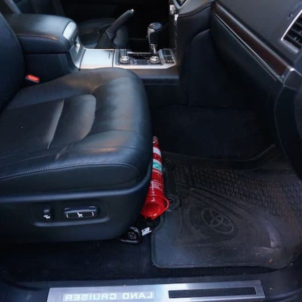 Toyota LandCruiser 200 Series cabin with a red fire extinguisher mounted on a KAP bracket at the base of the front seat