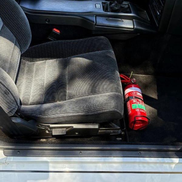 Toyota MR2 cabin with a red fire extinguisher mounted on a KAP bracket at the base of the front seat
