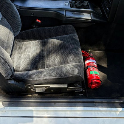 Toyota MR2 cabin with a red fire extinguisher mounted on a KAP bracket at the base of the front seat
