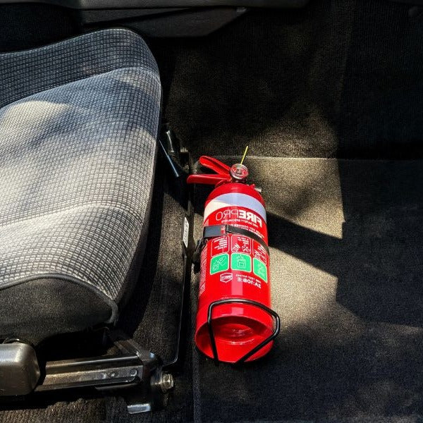 Close-up of a red fire extinguisher held in a KAP bracket at the base of the front seat in a Toyota MR2