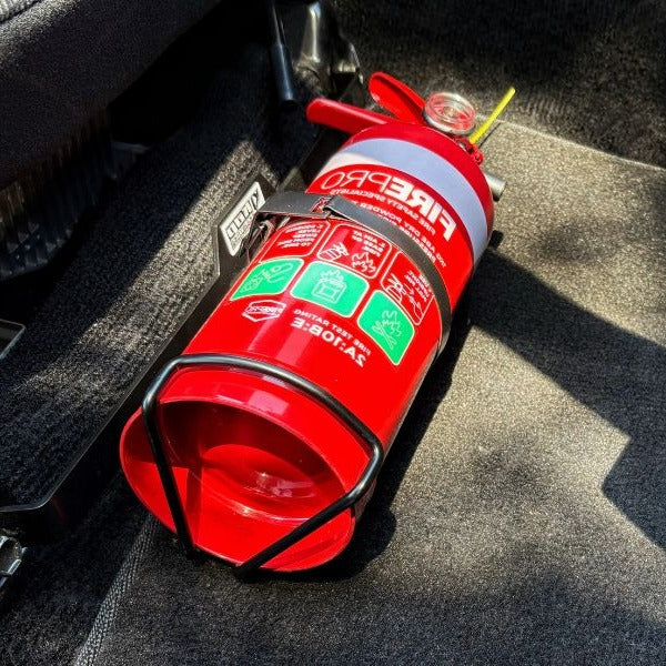 Close-up of a red fire extinguisher held in a KAP bracket at the base of the front seat in a Toyota MR2