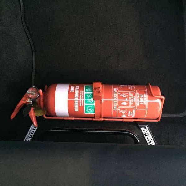 Close-up of a red fire extinguisher held in a KAP bracket at the base of the front seat in a Volvo C30