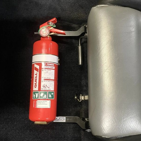 Close-up of a red fire extinguisher held in a KAP bracket at the base of the left front seat in a Nissan 300ZX
