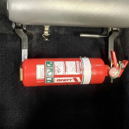 Close-up of a red fire extinguisher held in a KAP bracket at the base of the left front seat in a Nissan 300ZX