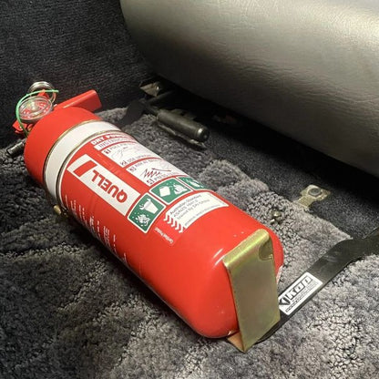 Close-up of a red fire extinguisher held in a KAP bracket at the base of the left front seat in a Nissan 300ZX